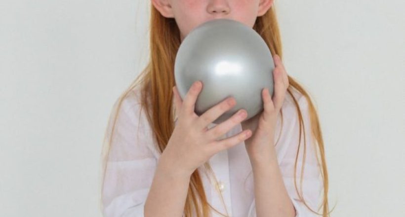 charming girl with red hair inflating gray balloon