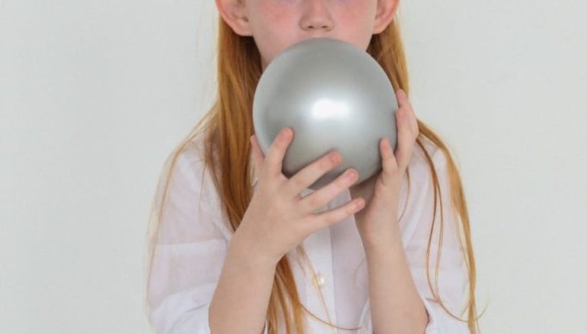 charming girl with red hair inflating gray balloon