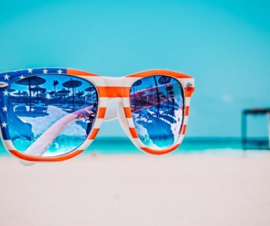 focus photography of american flag accent wayfarer styled sunglasses with sea background