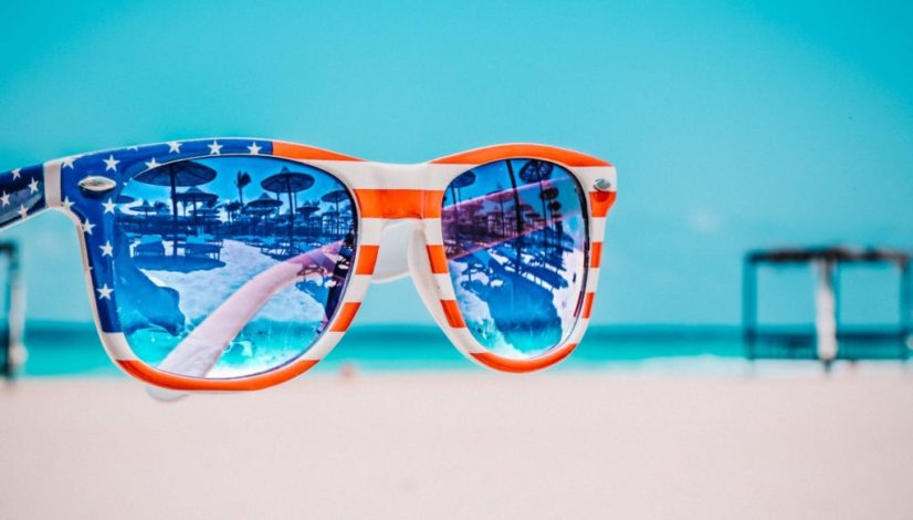 focus photography of american flag accent wayfarer styled sunglasses with sea background